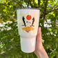 A hand holding a white insulated tumbler featuring a sticker of two Secretarybirds under a red sun on a beige background.